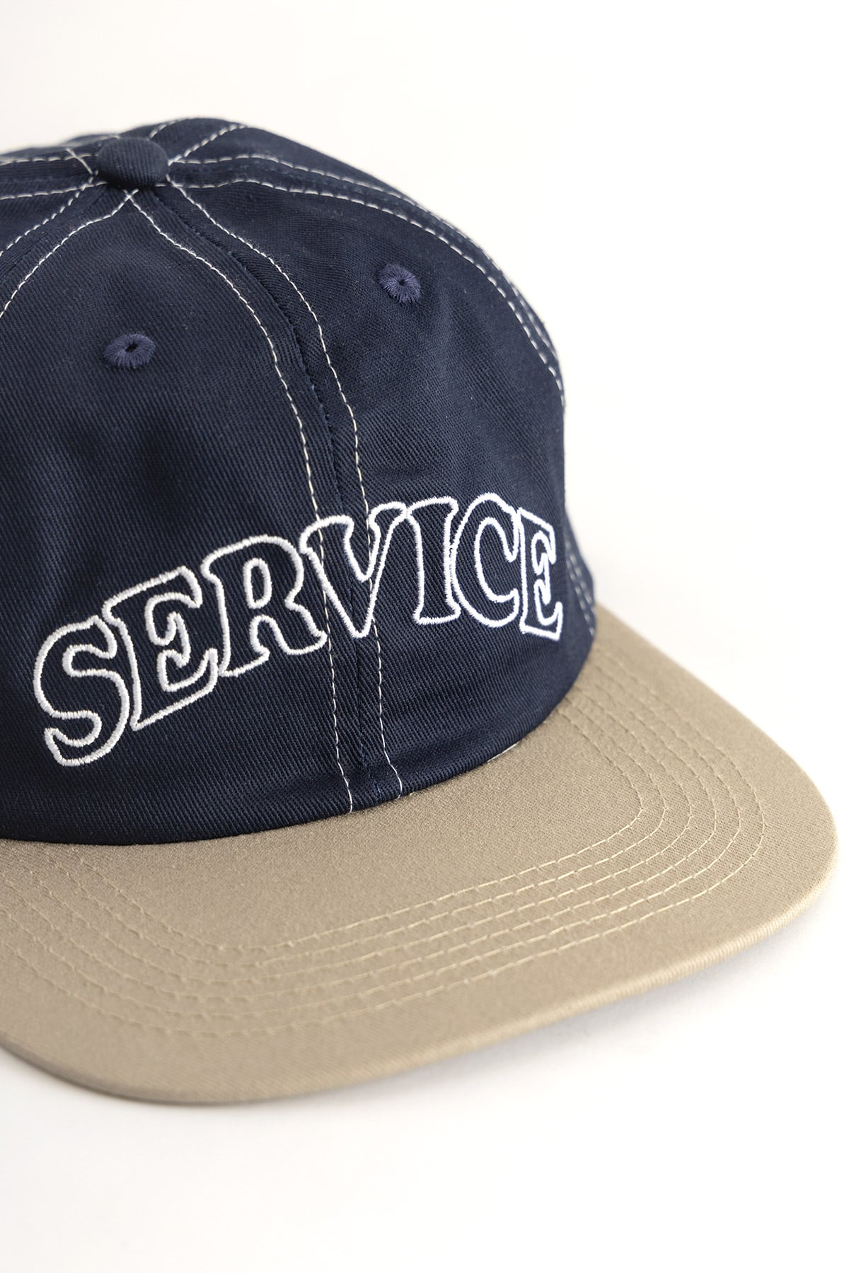 Side angle view of navy and khaki 6-panel cap with embroidered Arch Logo and contrast stitching detail