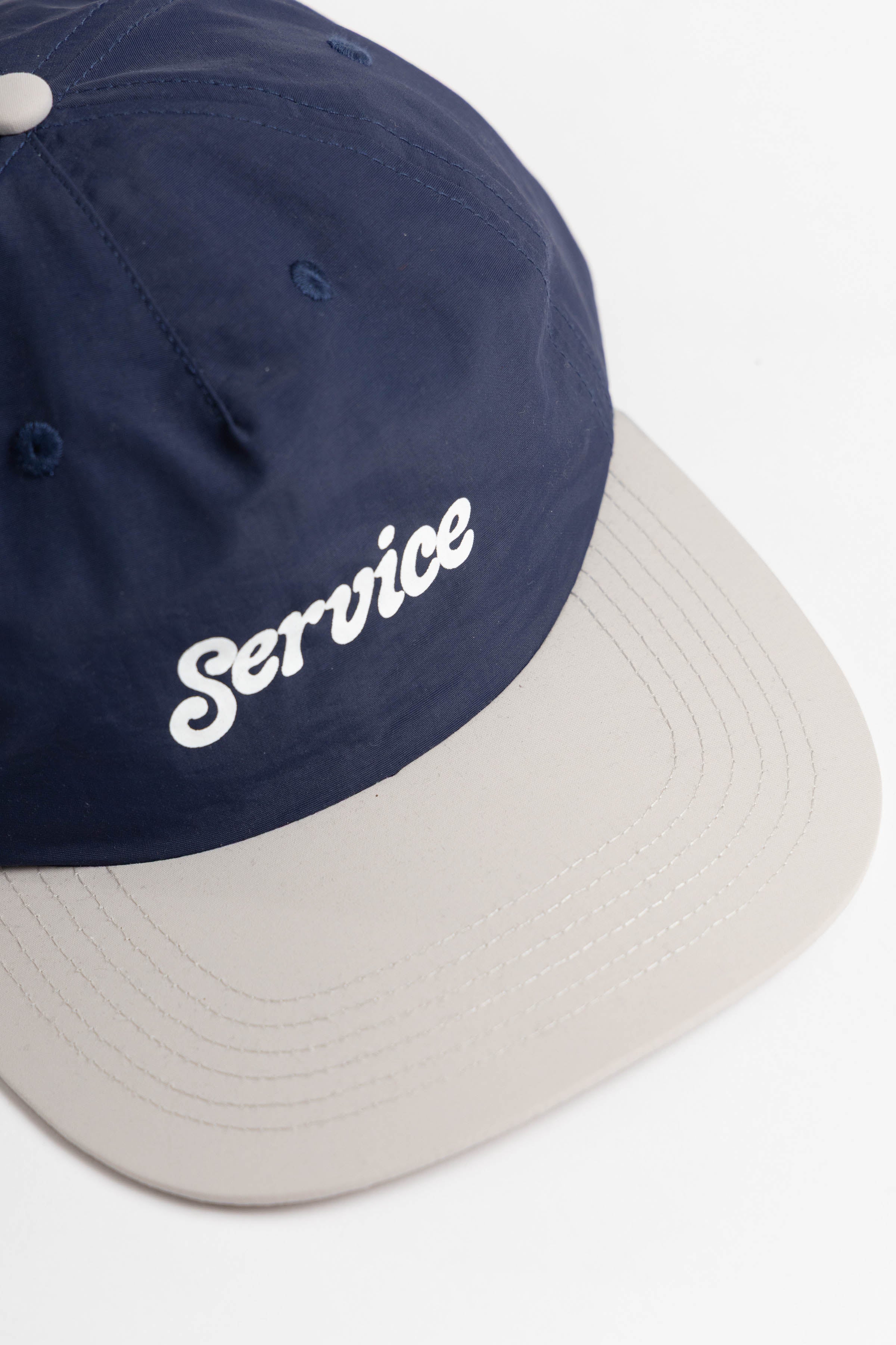 Model wearing Script Surf Cap in navy and off-white made from 100% cotton with low-profile fit, curved brim and elastic adjuster