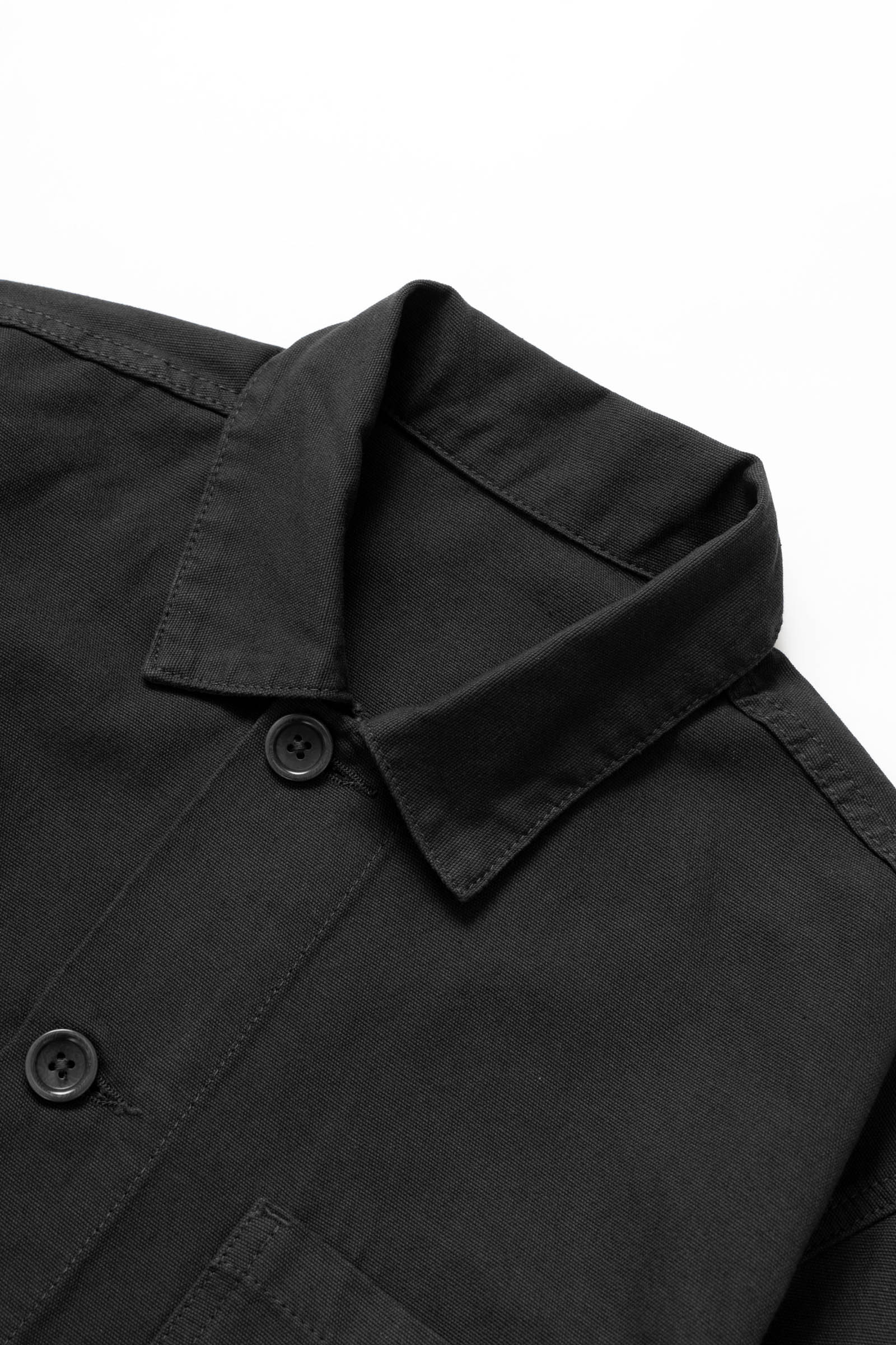 Close-up detail of the Service Works Canvas Chore Shirt in Black showing durable canvas texture and woven logo label.