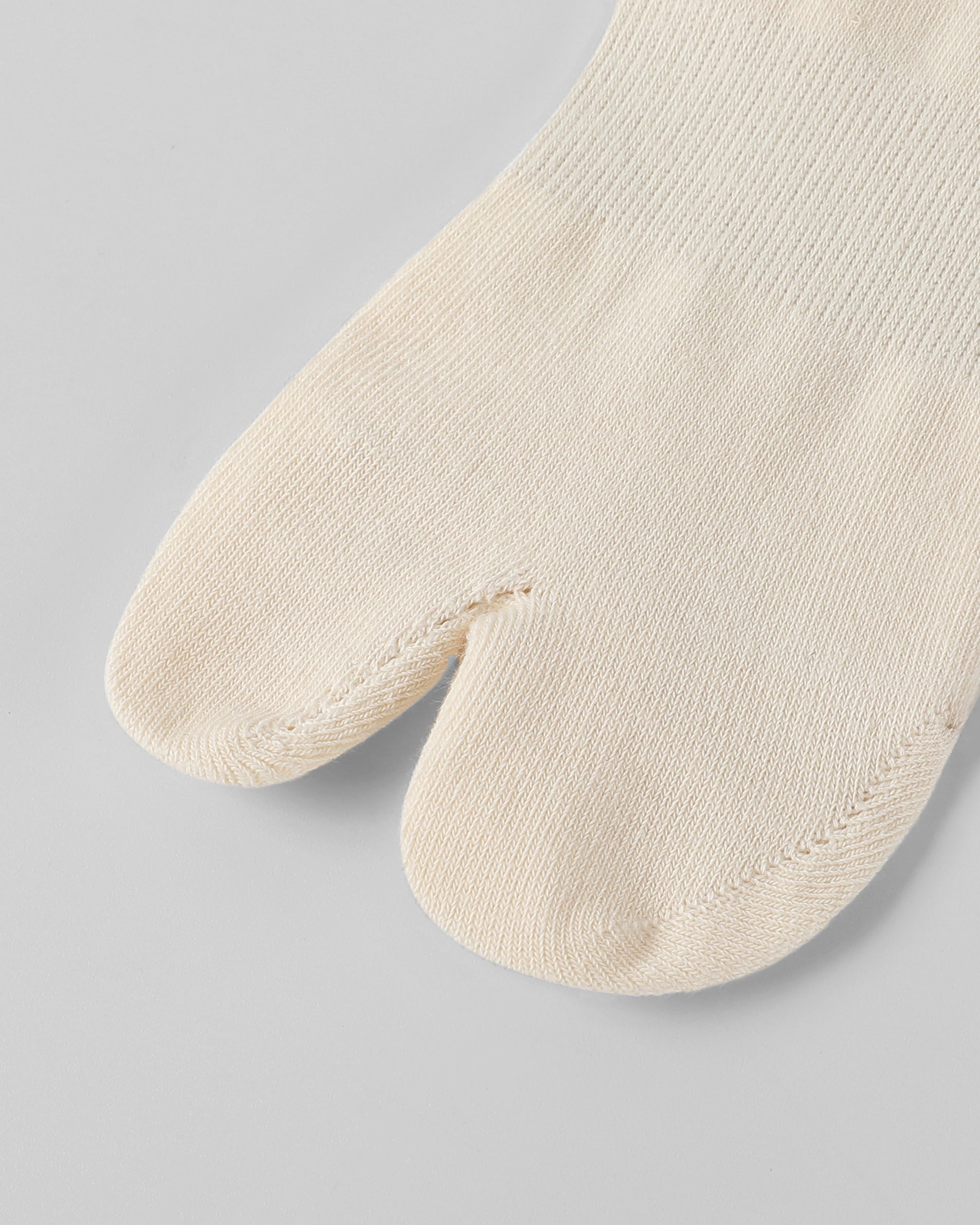 Model wearing off white tabi split-toe socks made from cotton blend fabric with stretch fit for breathable everyday comfort.