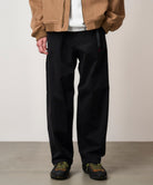 Side view of model wearing Cliff Pant Black stretch twill utility pants with relaxed fit, elastic waistband and nylon cinch belt