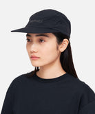 Side view of model wearing Gramicci Nylon Cap Black with recycled quick-dry nylon, five-panel construction and adjustable drawcord fit.