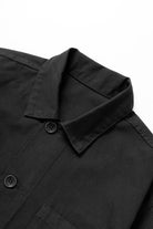 Close-up detail of the Service Works Canvas Chore Shirt in Black showing durable canvas texture and woven logo label.