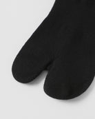 Model wearing black tabi split-toe socks made from cotton blend fabric with stretch and breathable everyday comfort fit.
