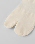 Model wearing off white tabi split-toe socks made from cotton blend fabric with stretch fit for breathable everyday comfort.