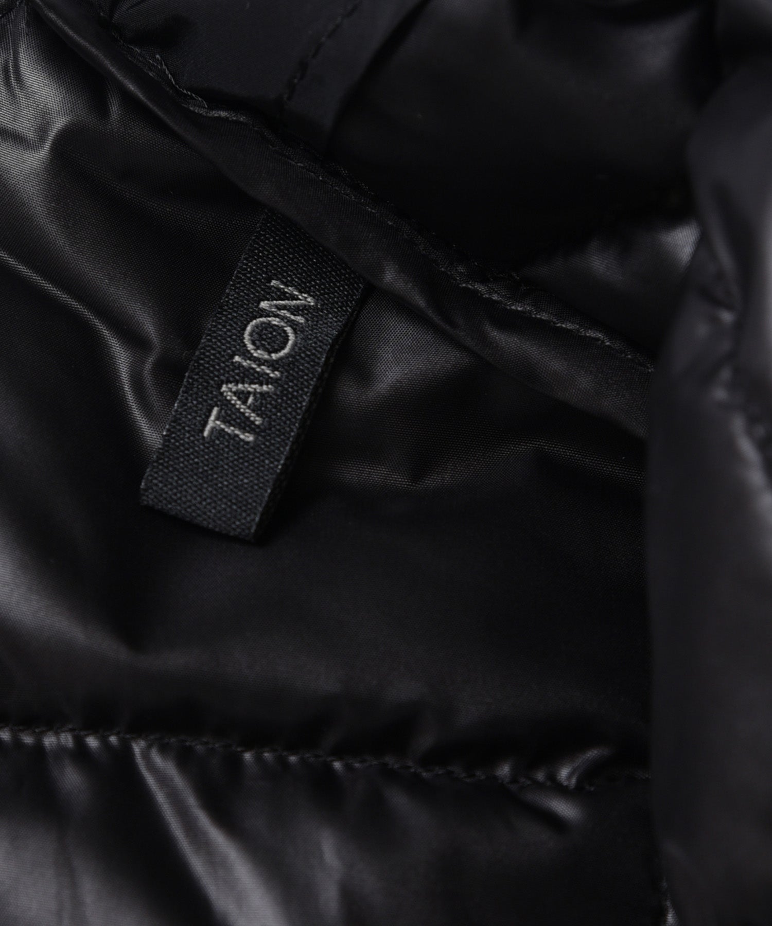 Close-up name tag detail of Taion Hi Neck W-Zip Down Jacket in Off White with premium branding finish